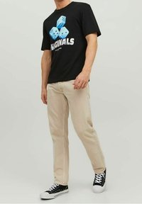 Svart t-shirt med blå tärningsgrafik och vit text, kombinerad med ljusbeiga jeans och svarta sneakers med vita sulor.