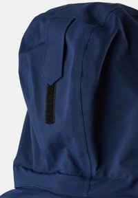 Marine stoffen capuchon met een gladde textuur, voorzien van een bovenklep en een zwart lusdetail voor aanpassing, met de nadruk op functionele designelementen.