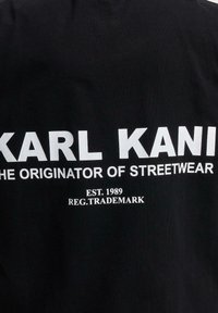Black cotton t-shirt featuring bold white text: "KARL KANI THE ORIGINATOR OF STREETWEAR" with "EST. 1989" and "REG. TRADEMARK" below.