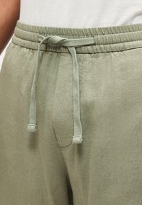 Κοντινό πλάνο ανοιχτοπράσινου φόρμας με κορδόνι στη μέση, φορεμένο με λευκό πουκάμισο.