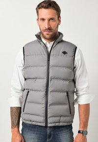 Graue Steppweste mit hohem Kragen, ausgestattet mit einem Frontreißverschluss und seitlichen Taschen. Besonders auffällig ist die gesteppten Textur und die schwarzen Akzente.