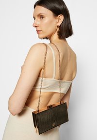 Metaliczna zielona kopertówka z łańcuszkiem, z teksturowanym wzorem węża i prostokątnym kształtem. Zamek na górze.