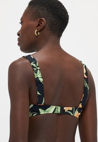 Top bikini nero con motivi floreali verdi e arancioni, dotato di spalline regolabili e chiusura con gancio sul retro.