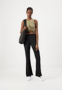 Olive green cropped top with twisted front, high-waisted black flared pants, and white sneakers. The model carries a dark shoulder bag.