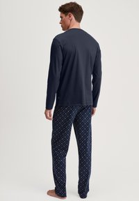 Herren Oberteil in Marineblau mit langen Ärmeln und Rundhalsausschnitt, kombiniert mit gemusterten Schlafanzughosen mit geometrischen Designs in Rosa und Weiß.