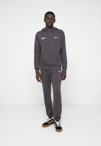 Sweatshirt cinza com capuz e bolso canguru, combinado com calças de moletom à condizer. Detalhes notáveis do logotipo em verde menta, ténis em preto e branco.