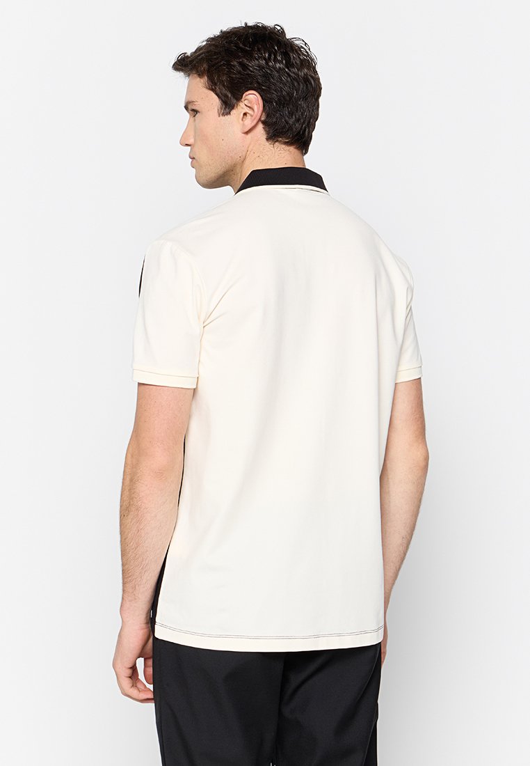 Kurzärmliges Poloshirt in Creme mit schwarzem Kragen, glatter Textur und kontrastierenden Schulterakzenten. Rückansicht zeigt die taillierte Passform.