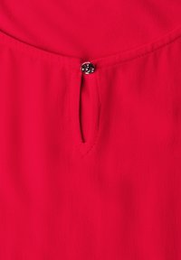 Tissu rouge avec un décolleté en forme de trou de serrure fermé par un petit bouton rond noir avec un motif floral découpé.