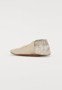 Beige fottøy med en jevn, avrundet tådesign. Har et blomsterprikket bakparti og elastisk ankel for en sikker passform. Lett såle.