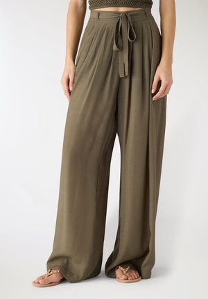 Pantaloni larghi a gamba larga color oliva con cintura annodata, indossati con sandali color cuoio con borchie e top corto a maglia.
