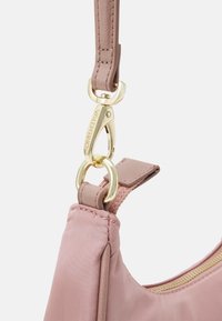 Pink fabric bag with a smooth texture, featuring gold hardware, a clip attachment, and a soft handle. Accents include stitching details.