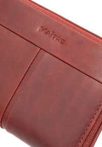 Red leather wallet with a smooth texture, zip closure, and embossed "MAITRE" logo. It features card slots and precise stitching details.