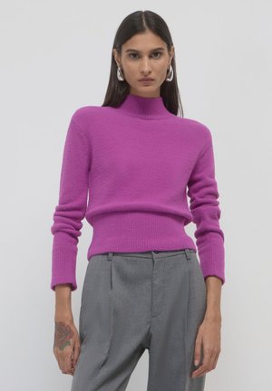 Maglione fucsia a maglia con colletto alto e polsini a costine, abbinato a pantaloni grigi chiari su misura. Morbida texture e design aderente.