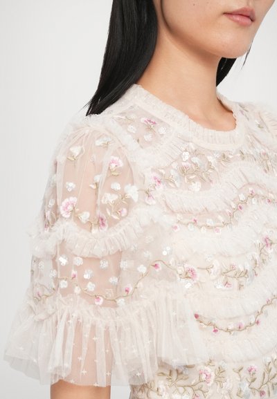 Svetloružová priehľadná blúzka s kvetinovou výšivkou a volánovými rukávmi. Obsahuje jemné trblietky a textúrovanú látku, vytvárajúcu vrstvený efekt.