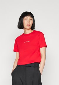 Red cotton t-shirt with crew neck and short sleeves, featuring a small white logo "Calvin Klein Jeans" on the chest. Smooth texture.