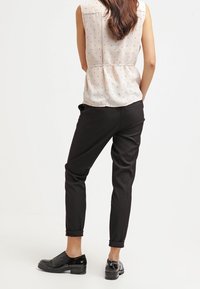 Černé zúžené kalhoty s ohrnutými manžetami, v kombinaci s bezrukávovým světlým topem s puntíkovaným vzorem. Oblečení doplňují černé boty.