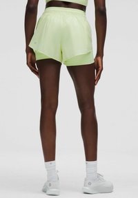 Helle grüne Sportshorts mit einem geschichteten Design, versehen mit einem elastischen Bund und einer glatten Textur. Getragen mit weißen Sneakers und Socken.
