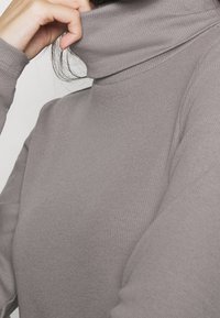 Grau gerippter Rollkragenpullover mit hohem Kragen und figurbetontem Design, das eine weiche Textur und lange Ärmel zeigt.