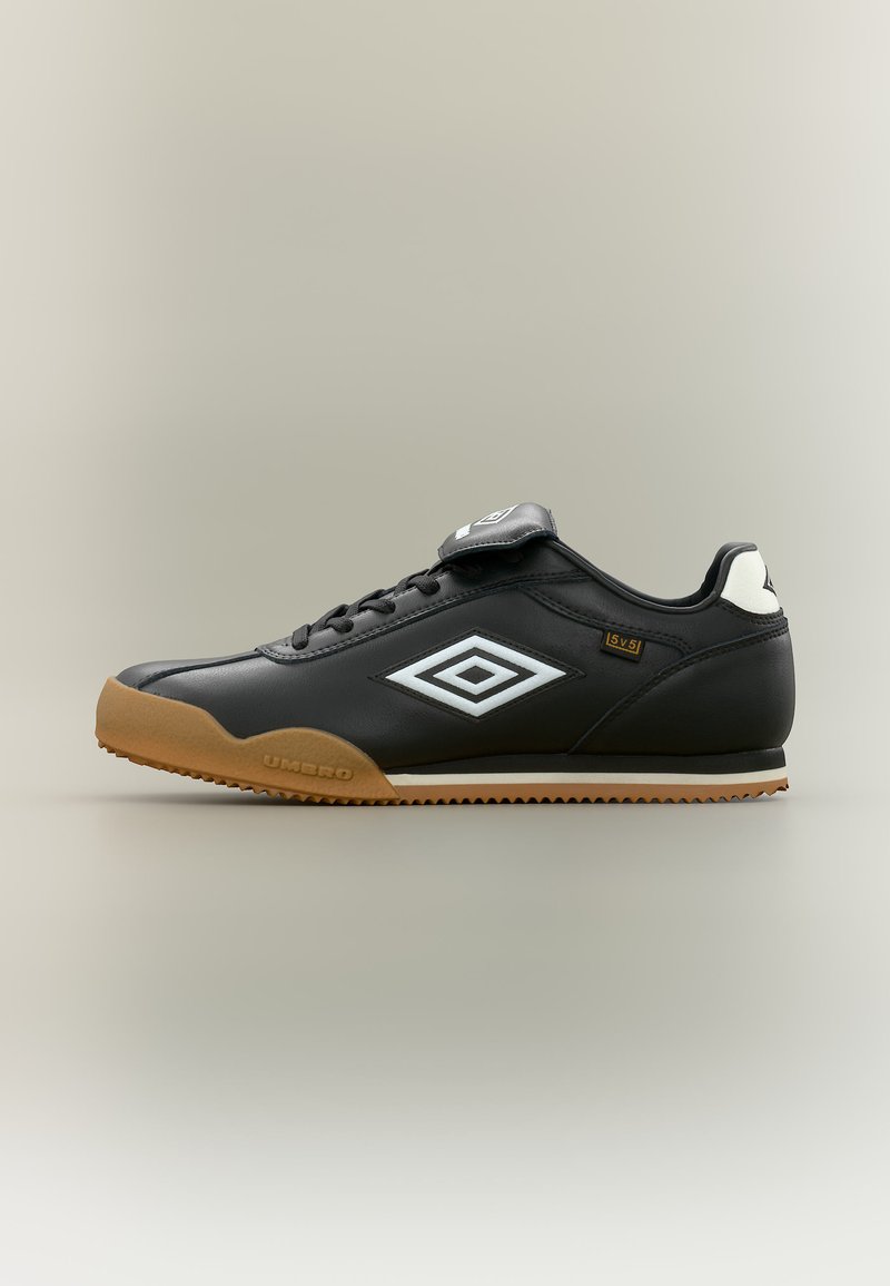 Μαύρο δερμάτινο sneaker χαμηλού προφίλ με λαστιχένια σόλα, λευκό λογότυπο Umbro στο πλάι, μαύρα κορδόνια και μια πτυχή πάνω από τη γλώσσα σε ουδέτερο φόντο.