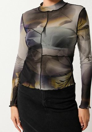 Haut transparent à manches longues avec imprimé floral abstrait sombre, coutures contrastantes noires et poignets à effet ondulé, associé à une jupe noire.