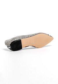 Zapato plano con un patrón en blanco y negro, punta redondeada, parte superior de cuero liso, tacón negro contrastante y suela de goma beige.