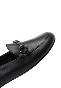 Zwart lederen loafer met een soepele textuur, scherpe neus en een decoratief hardwareaccent met een ronde lus op de bovenkant.
