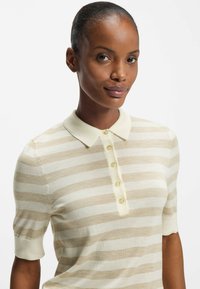 Polo a righe beige e crema, maniche corte, con una texture morbida e un collo con quattro bottoni rotondi.