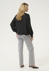 Blusa nera a maniche lunghe con spalle a palloncino, abbinata a jeans dritti grigio chiaro. Le décolleté nere con tacco completano l'outfit.