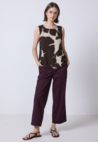 Haut sans manches avec un motif abstrait crème et marron, associé à un pantalon large bordeaux foncé. Porté avec des sandales noires à brides.