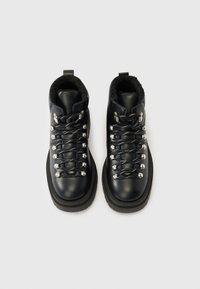 Bottes de randonnée noires en cuir, avec une doublure en peluche, des accessoires argentés et des semelles épaisses en caoutchouc. Lacets ornés d'accents métalliques.