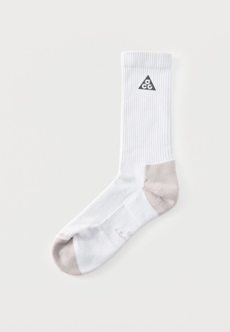 Chaussette blanche mi-haute avec bout et talon gris, texture côtelée, et un logo triangulaire noir près du haut avec les lettres "acg" à l'intérieur.