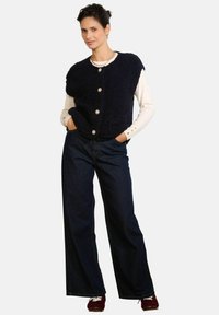 Jūras zila pūkaina veste ar lielām pogām uz krēmkrāsas garām piedurknēm topa, kombinēta ar plaša piegriezuma tumšā džinsa biksēm. Aksesuāri ietver pērļu kaklarotu.