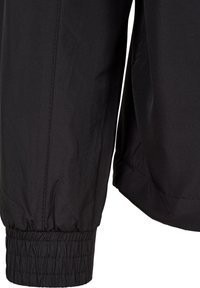 Gros plan d'une manche de veste noire avec un poignet élastique et des détails de couture visibles sur un tissu lisse.