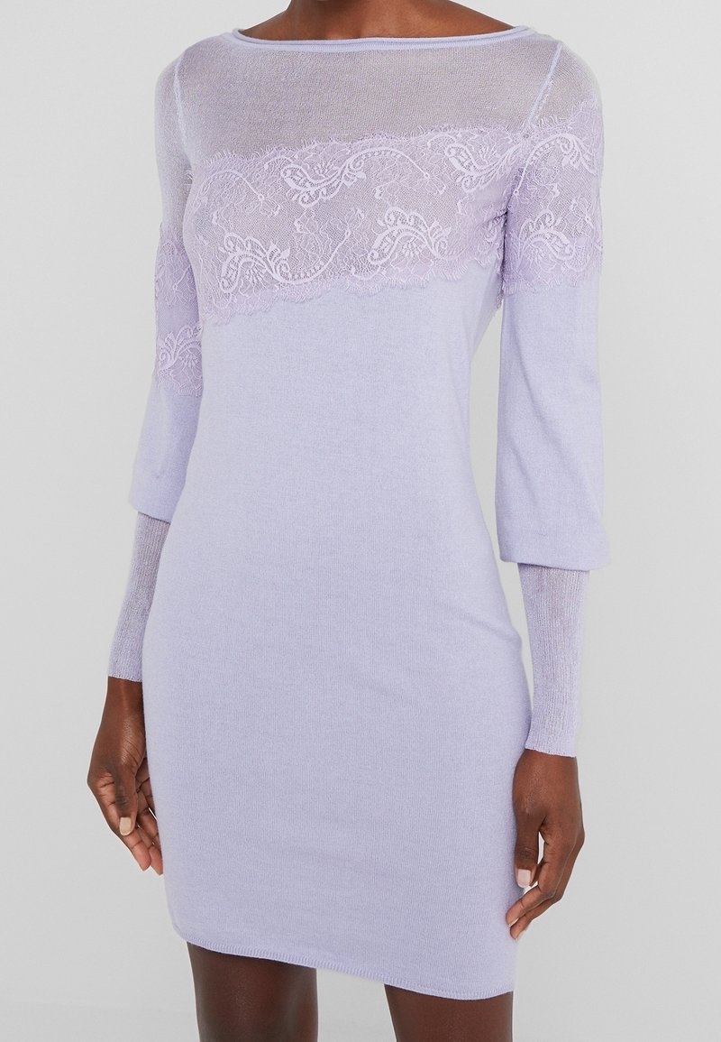 Vestito lavorato a maglia lilla con top in rete trasparente e dettagli in pizzo sul petto. Ha maniche a tre quarti e una silhouette aderente.