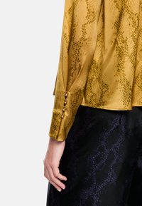 Long-sleeve shirt in mustard yellow satin with a snake print pattern; features decorative buttons on cuff and a relaxed fit.
