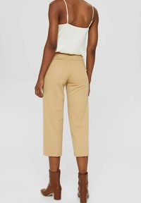 Pantalon court beige à coupe droite, associé à un haut à bretelles fines vert clair. Bottines marron. Texture de tissu lisse.