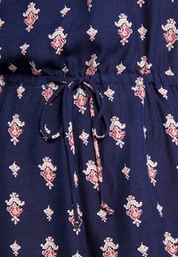 Tissu marine avec un motif floral rouge et crème, doté d'une taille élastique avec un lien de serrage pour un ajustement personnalisé.