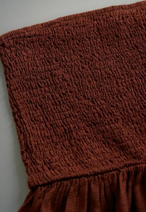 Tkanina v rustikálnej farbe s textúrovaným, zvrásneným vzorom; má smockovaný vrch a nazhromaždený volánový spodný lem.