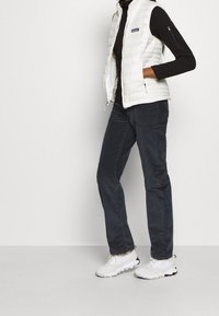 Vit puffväst över en svart polotröja, kombinerad med mörka byxor och vita sneakers. Funktioner inkluderar dragkedjefickor och ett quiltat mönster.