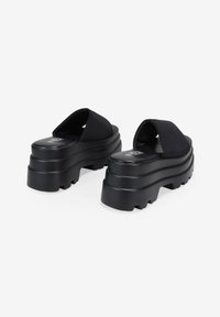 Sandalias de plataforma negras con suela texturizada, que cuentan con suaves correas de tela y un diseño voluminoso y estratificado para altura y estabilidad.