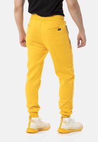 Gelbe Sweatpants mit einem elastischen Bund und seitlichen Taschen. Hergestellt aus weichem Material, mit einem schlanken Schnitt und gerippten Bündchen.