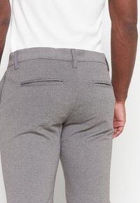 Gray tailored pants with a textured fabric, featuring two back pockets with subtle stitching and a smooth waistband.