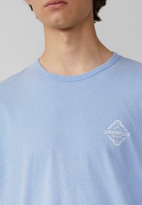 Lichtblauw katoenen t-shirt met korte mouwen en een ronde hals. Bevat een klein wit geborduurd logo aan de linkerkant.