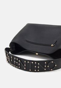 Black leather handbag with a curved flap, zip closure, and a bold, studded strap featuring raised lettering. Smooth texture with metallic accents.