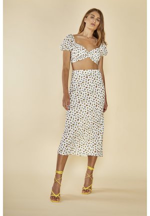 Conjunto de dos piezas que presenta una blusa blanca corta con mangas abullonadas y una falda midi a juego, ambas adornadas con un patrón floral multicolor. Sandalias amarillas con tiras.