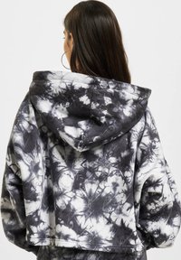 Juoda ir balta tamsiuoju tie-dye raštu su kapisonu, oversized dydis. Medžiaga atrodo minkšta, pasižyminti subtiliais raštais visame paviršiuje.