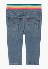 Pantalones de mezclilla para niños en azul con dos bolsillos traseros y una cinturilla elástica con rayas de arcoíris en colores verde azulado, amarillo, naranja y rosa.