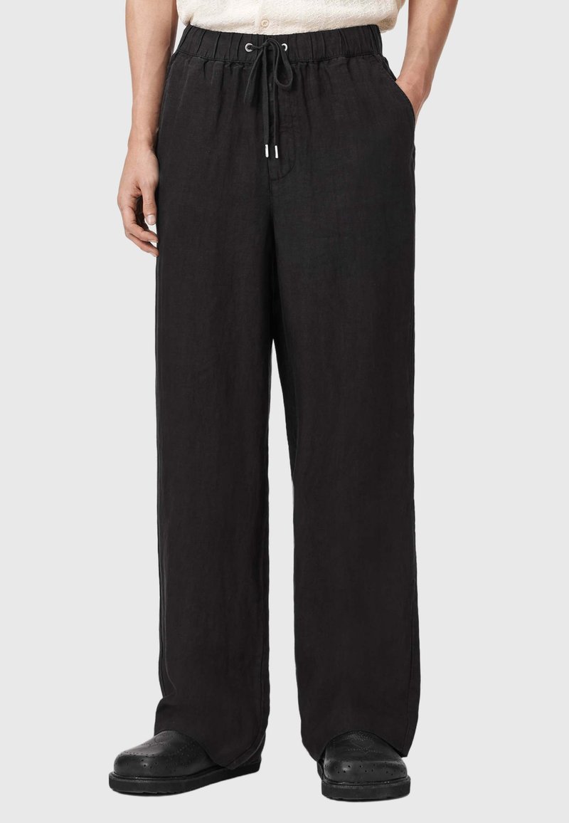 Schwarze Leinenhose mit lockerem Schnitt, elastischem Bund und Kordelzugverschluss. Mit Seitentaschen und glatter Textur.