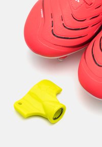 Le scarpe da calcio rosse presentano una parte superiore testurizzata con accenti neri e tacchetti trasparenti, abbinate a uno strumento per tacchetti di colore giallo brillante.