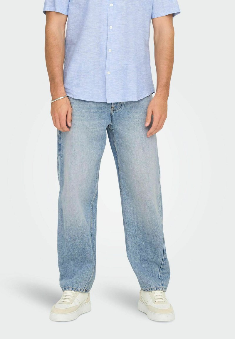 Ljust blå knäppt skjorta med korta ärmar, ihop med löst sittande, blekta blå jeans och vita sneakers. En enkel och avslappnad outfit.
